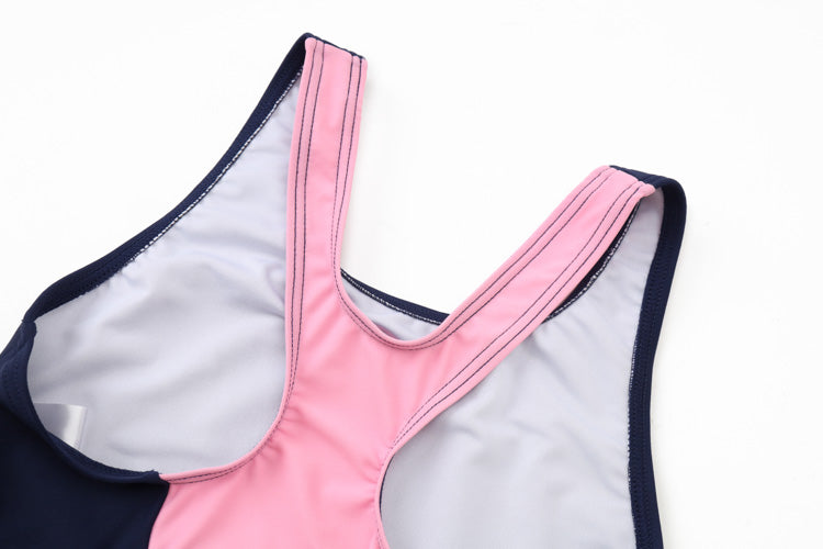 A close-up of the 寶藍色女童練習泳衣 <68400464-Y1>, a sleeveless top with navy and pink panels, white lining, neat seams, and made from 彈性布料, laid flat on a white surface.